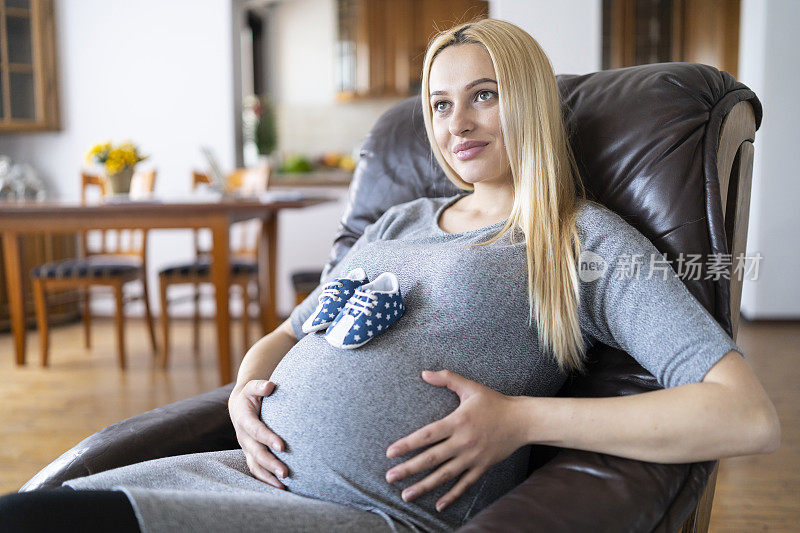 孕妇坐在沙发上，婴儿趴在肚子上