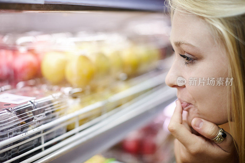 金发购物者从超市冰箱中选择水果