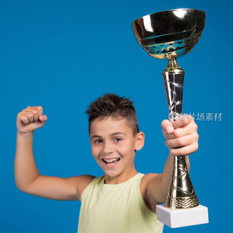 快乐的男孩是胜利者，他把一个大的体育杯举过头顶，笑着说，胜利者的概念