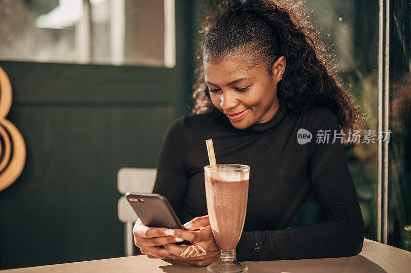 一名黑人女性独自坐在路边的咖啡馆里用着智能手机