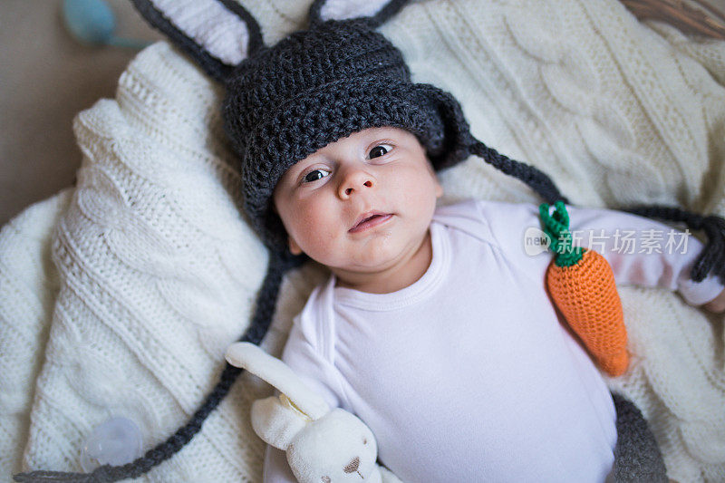 刚出生的小男孩戴着兔耳朵和尾巴，放在篮子里。