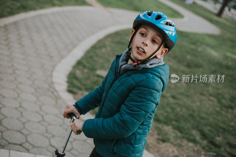 小男孩在外面骑着他的踏板车，面带微笑