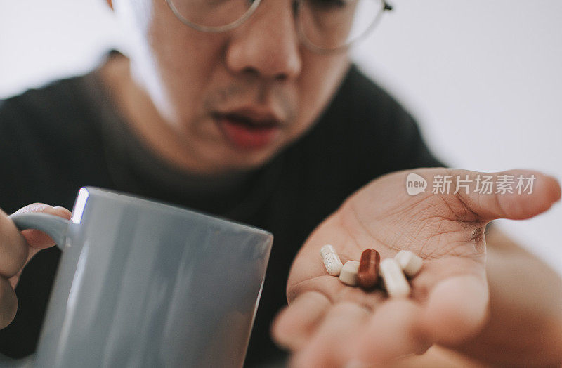 一位患有流感症状的亚洲华人中年男子正在服用以手掌药为主的药丸
