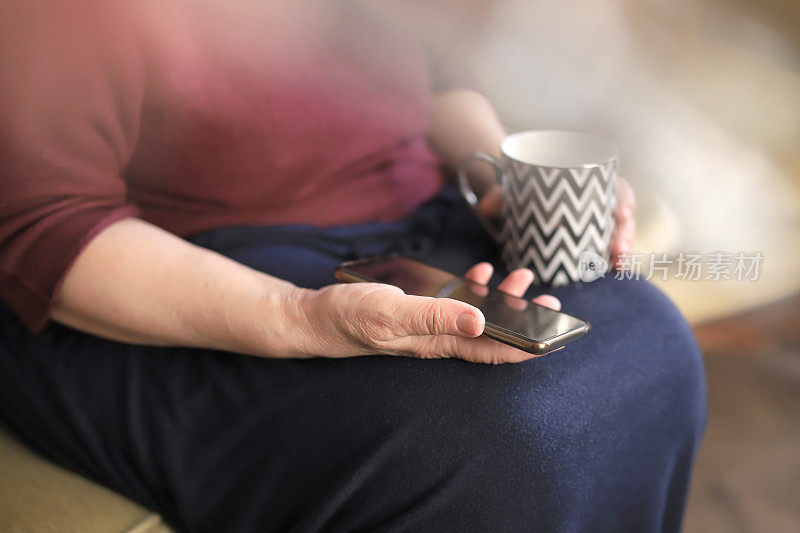 不知名成熟女人的手拿着咖啡杯和手机