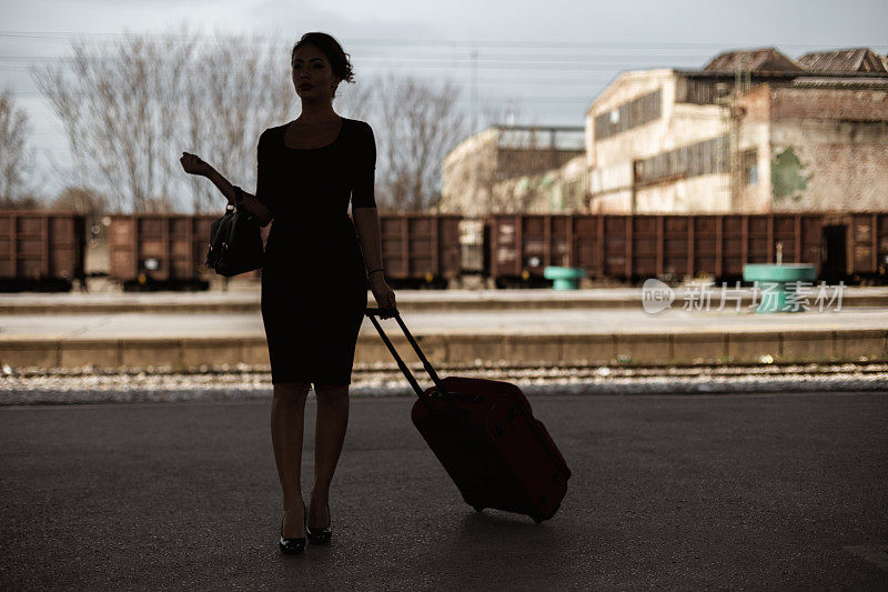 一个年轻女子提着手提箱在车站等火车