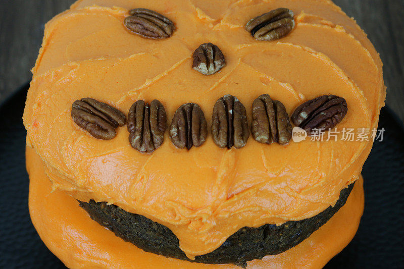 自制的万圣节南瓜脸巧克力蛋糕与橙子黄油奶油和核桃，杰克灯脸蛋糕的特写图像，高视点