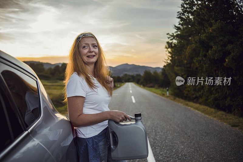 一位妇女在路上试图修理一辆坏了的汽车。这位妇女给她的车加油，试图继续旅程。一个女人带着一桶汽油在一辆车旁边