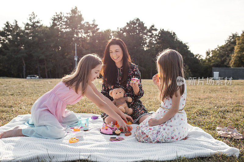 妈妈两个女儿和泰迪熊在公园里享受