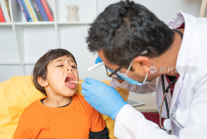 经验丰富的男儿科医生在家访时在客厅用木制压舌板和手电筒检查小儿喉咙。