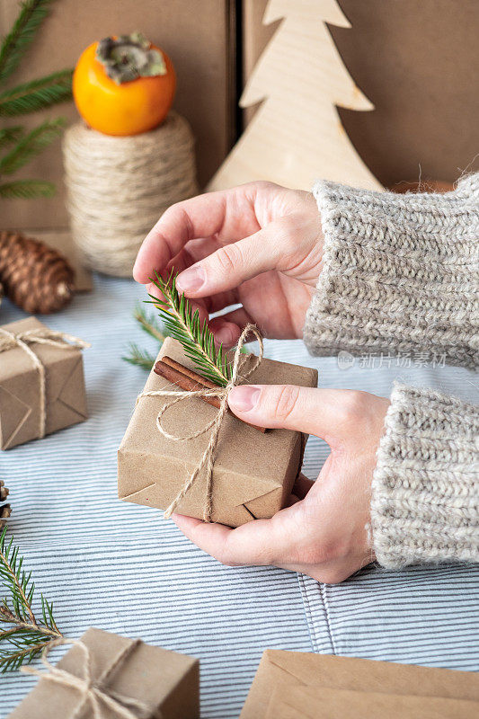 为圣诞节和新年包装时尚的现代礼物的过程。用牛皮纸、麻绳和圣诞树树枝做成的礼盒。圣诞背景，节日氛围