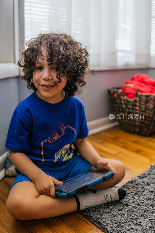 小男孩坐在地板上用平板电脑玩电子游戏