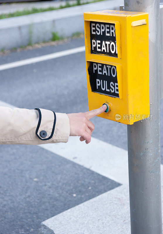 一个女人的手指按下了交通灯的行人按钮。出现的单词意思是:“等待行人”，“按行人”。