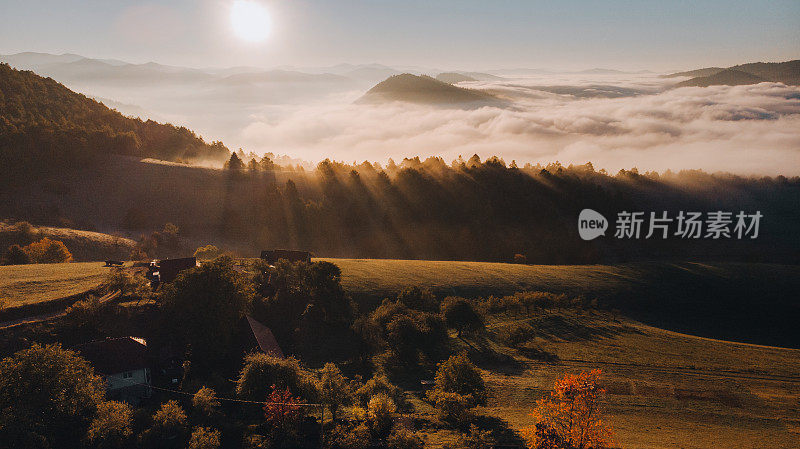 在雾蒙蒙的山间，秋天里，山顶上一座小乡村房屋上方的美丽日出