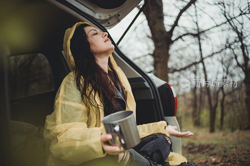 一个快乐的年轻女子在一个下雨天穿着一件黄色雨衣在树林里享受大自然。