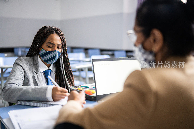 十几岁的学生在教室里和老师一起学习，戴着口罩