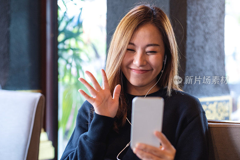 一个年轻的亚洲妇女挥手的肖像图像，同时使用手机视频电话