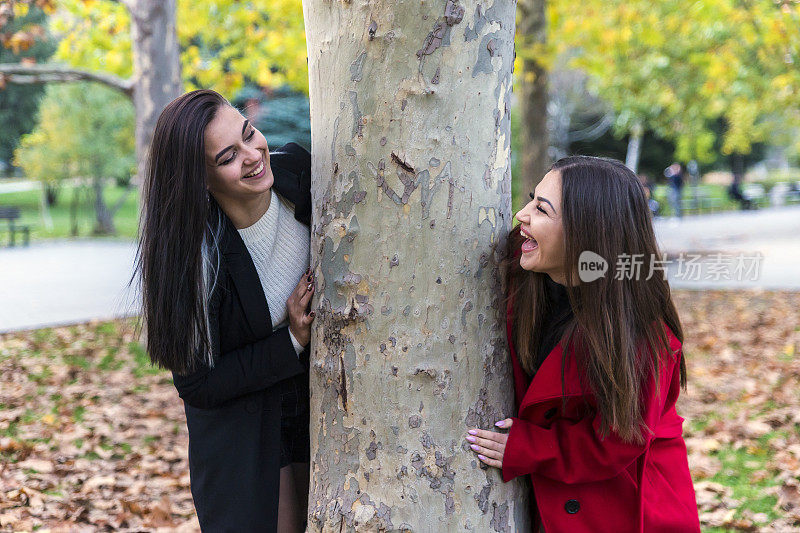 两个漂亮的年轻女子在公园里用手机拍照，