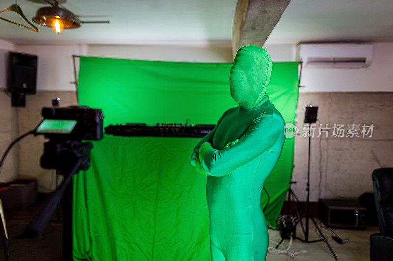 在绿色屏幕前，一名身穿绿色西装、面目不明的男子被摄像机记录了下来
