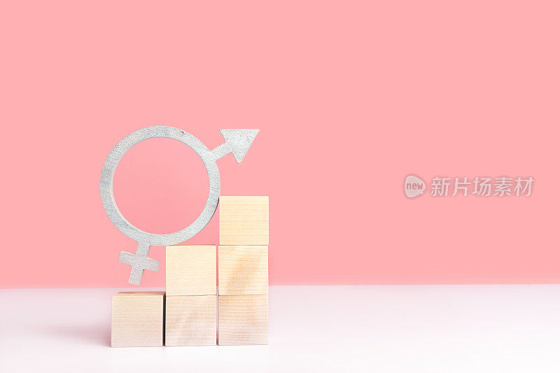性别平等的概念，模型在一个粉红色的背景与文本空间。银色的性别平等的象征矗立在金字塔阶梯状的木制立方体上。