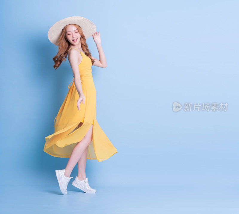 年轻的亚洲女子在蓝色背景下穿着黄色连衣裙的全长图像