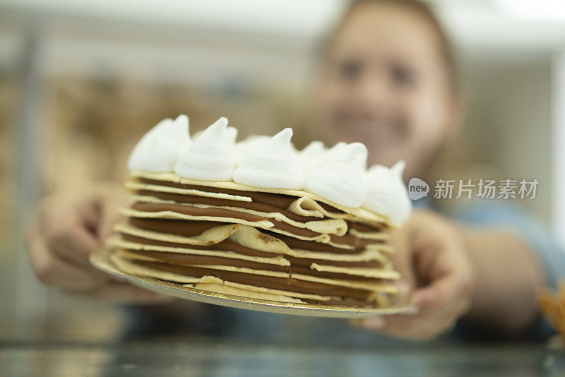 一名快乐的女性面包店员工的肖像显示蛋糕在商店柜台