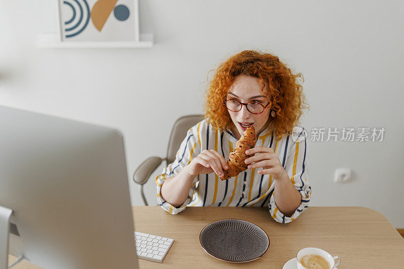 女人在办公室工作时吃牛角面包