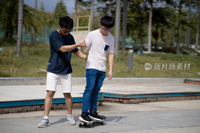 亚洲中国少年在滑板公园教他的弟弟玩滑板