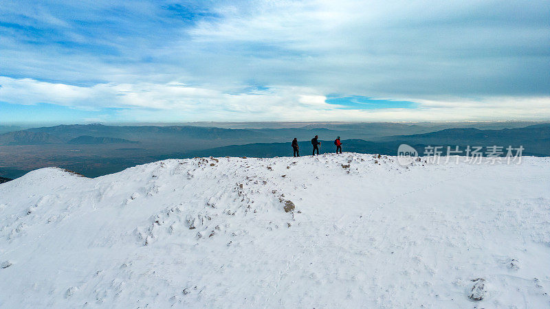 无人机拍摄的成功登山队在冬季雪山山顶的山脊上排成一行行走