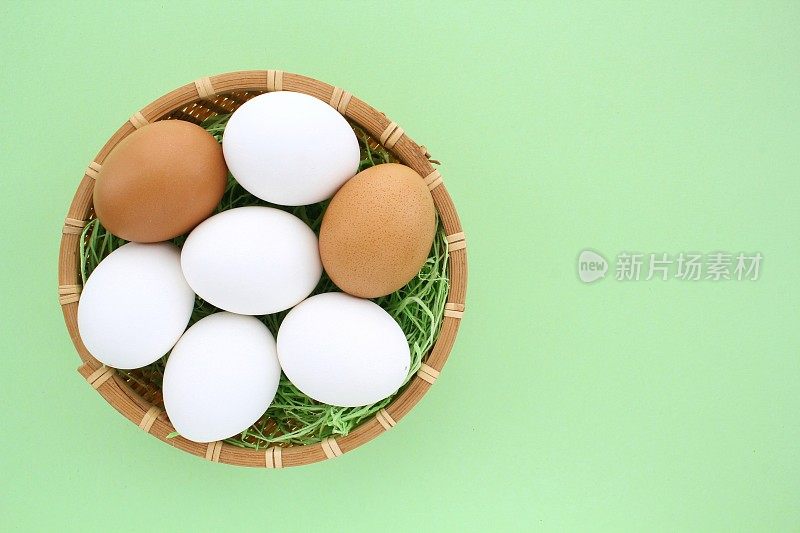 新鲜的鸡蛋在木制藤条篮子在绿色背景。天然健康营养有机农家食品产品理念