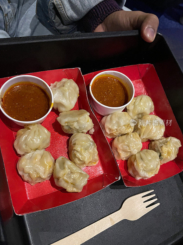 图片上是两盘蒸熟的Momos(南亚饺子)，白面粉和水面团，馅料是猪肉和混合蔬菜，放在红色纸板盘子上，作为蘸酱的电影院小吃