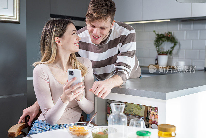 一对年轻夫妇边吃早餐边玩手机。星期天早上在家里。