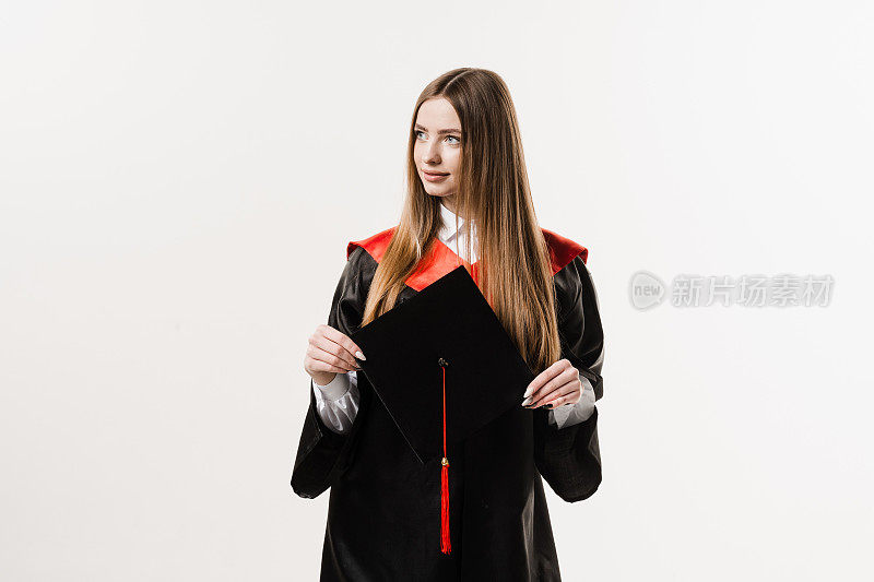 身着黑色毕业服的硕士女研究生手持白底帽。年轻迷人的女子大学毕业。