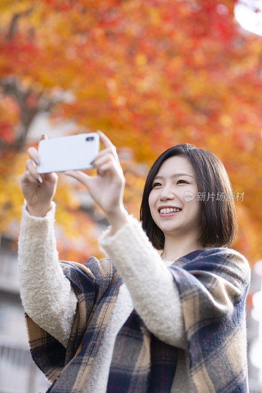 一名女子正在用智能手机拍摄秋天的树叶
