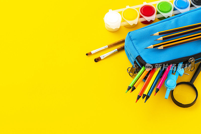学习用品:装满彩色铅笔的铅笔盒、绘画指南针、颜料和黄色背景的放大镜。本空间