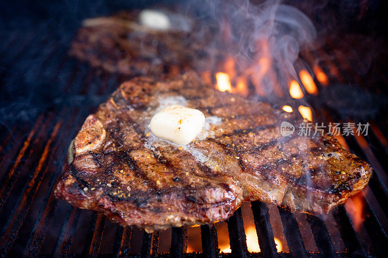 在火焰烤架上完美烹饪的t骨牛排，上面放上一团黄油，是一顿令人垂涎的大餐，满足了任何食肉动物的渴望