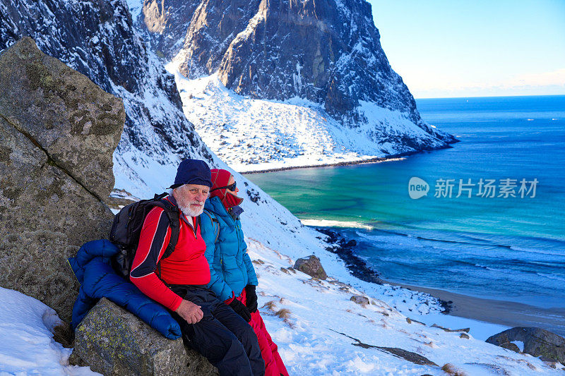 老年人，男人和女人，在山口休息，同时欣赏挪威罗弗敦群岛Kvalvika海滩的景色。