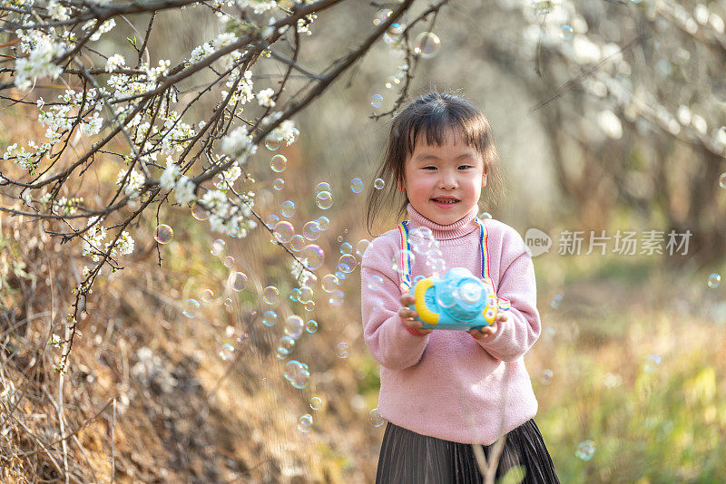 一个小女孩在盛开的梅树上吹泡泡