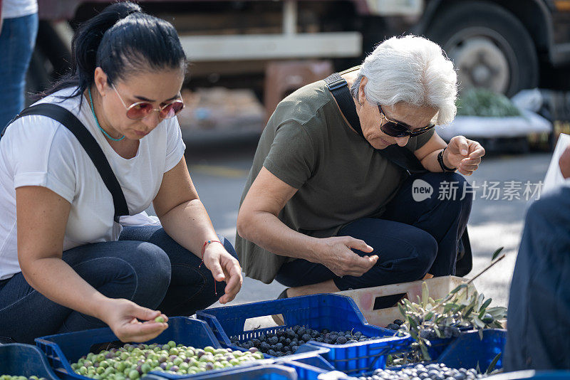 老年妇女和成年妇女在农贸市场购买新鲜橄榄的照片。