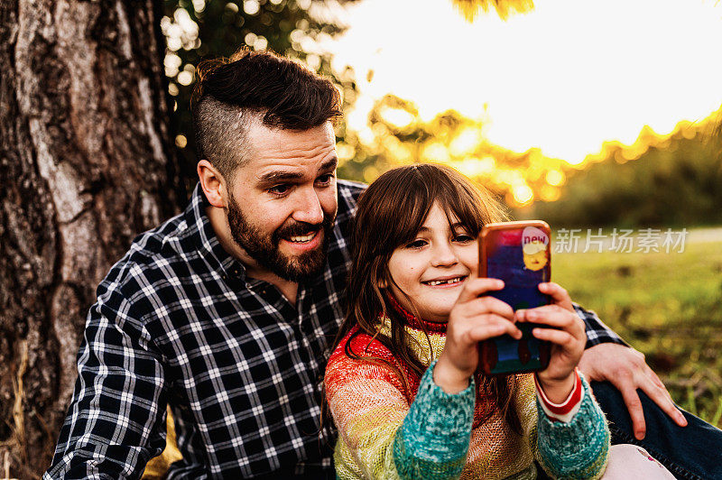 秋天，父亲和上小学的女儿用手机自拍，享受户外大自然的时光