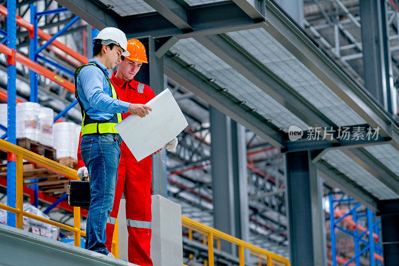 专业工程师手持图纸图纸，技术工人在工厂的铁轨旁停留讨论。