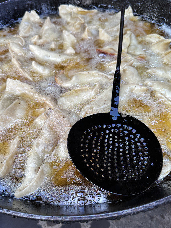 在karahi(印度炒锅)中油炸的一批samosas的特写图像，冒泡的热油，开槽的勺子，印度街头小吃摊，不健康的饮食，高架视图