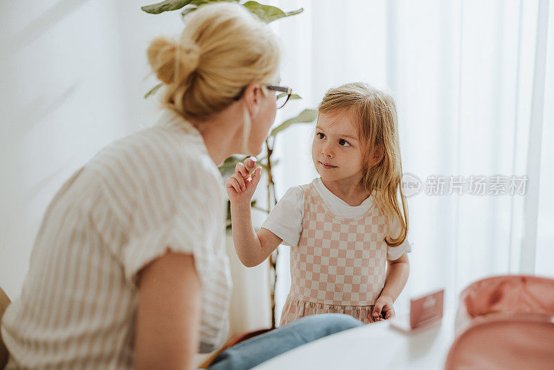 一个微笑的小女孩在家里给她不知名的妈妈涂口红的高视角