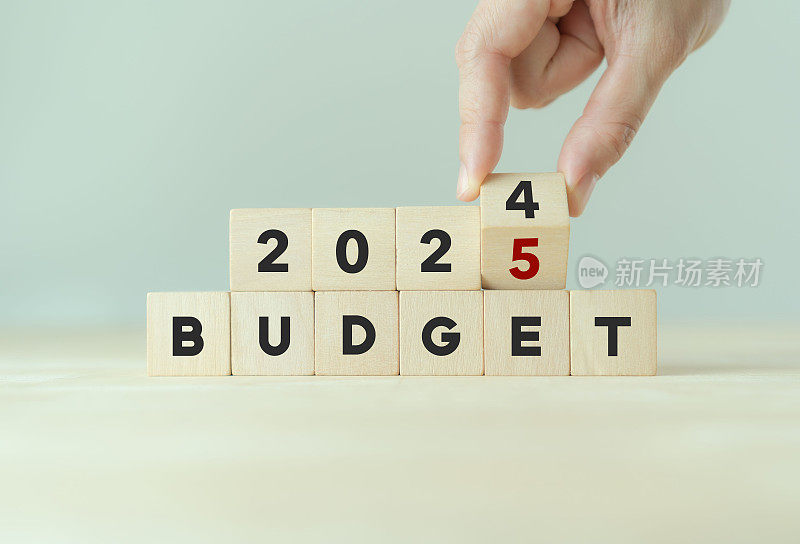 2025预算规划和分配概念。用手翻转木立方体，将“2024年预算”改为“2025年预算”，背景为灰色，拷贝空间。用于横幅和演示。