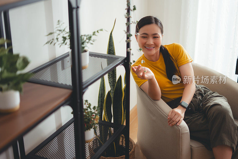 亚洲女性坐在家里客厅的扶手椅上享受放松时光。