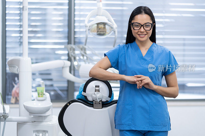 在现代化的牙科诊所办公室里，穿着制服，双臂交叉，微笑着看着镜头的亚洲女牙科工作者