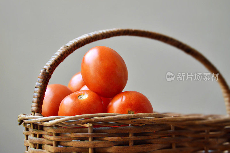 棕色的柳条篮子里堆满了一堆红熟的西红柿，灰色的背景上有把手，留下了复制空间，适合放蔬菜、素食食品农贸市场相关的海报、背景