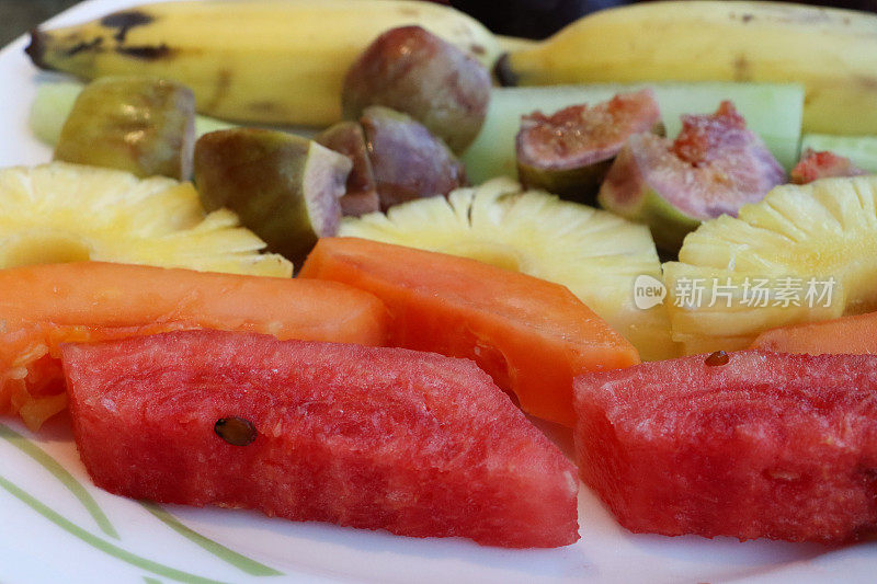 新鲜的全画幅图像，热带水果沙拉与一排排切片西瓜，木瓜，菠萝，无花果，瓜，香蕉和李子在白色盘子，重点在前景