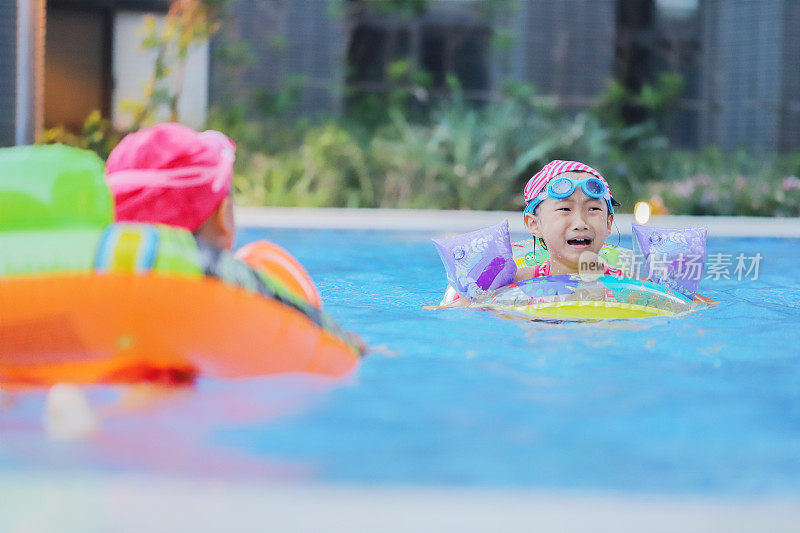 亚洲女孩在游泳池里玩水，同时练习如何游泳
