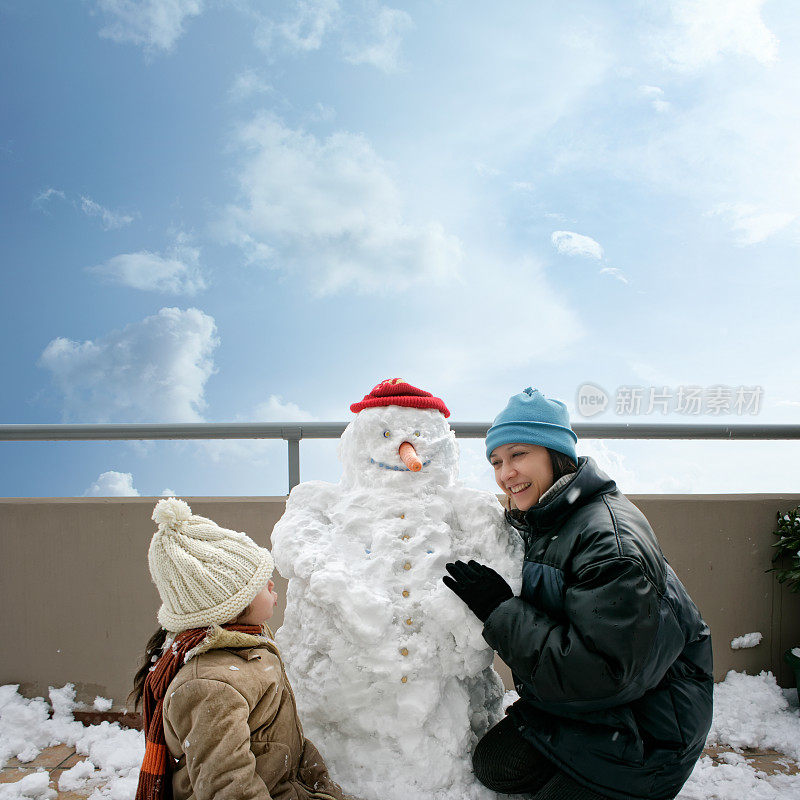 快乐的妈妈和女儿在阳台上玩雪人