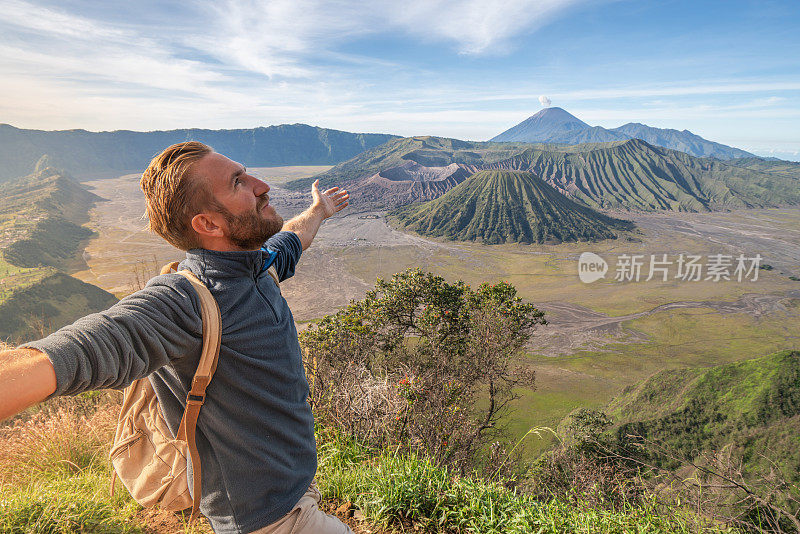 在印度尼西亚，年轻人徒步旅行，手臂伸开站在火山的山顶上，人们旅行的乐趣，冒险的概念，成功和成就